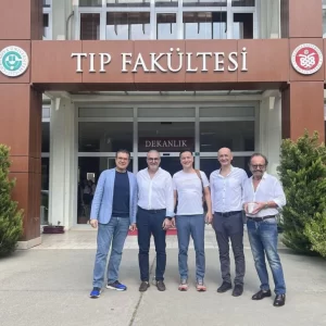 Dr. Göksel standing with fellow physicians in front of a Turkish medical faculty building.