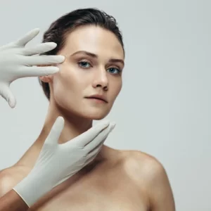 Woman in gloves examining her facial contours, representing facial aesthetics procedures.